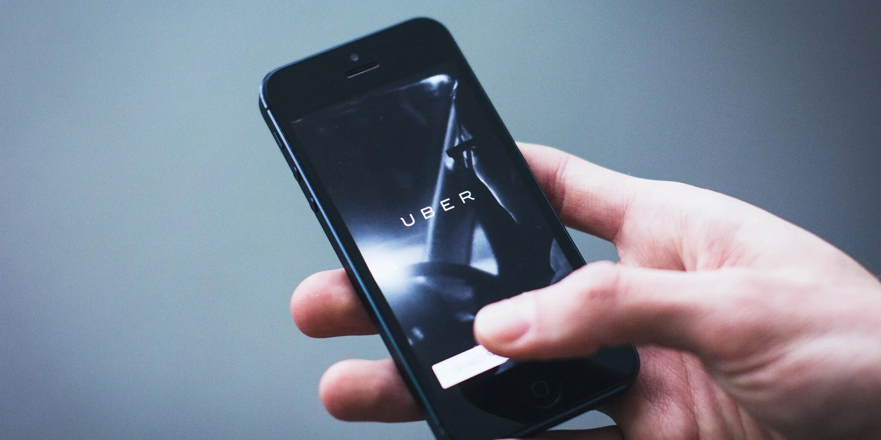 Hand holding a smartphone displaying the Uber app logo