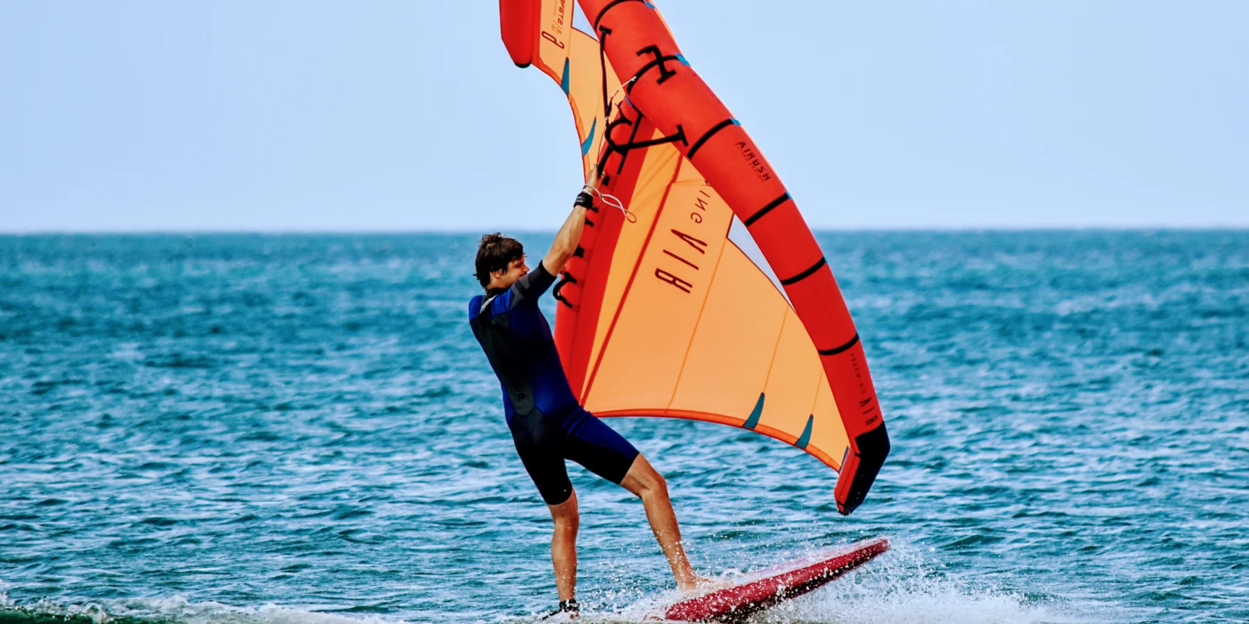 Wing foiler gliding over the ocean with an orange wing