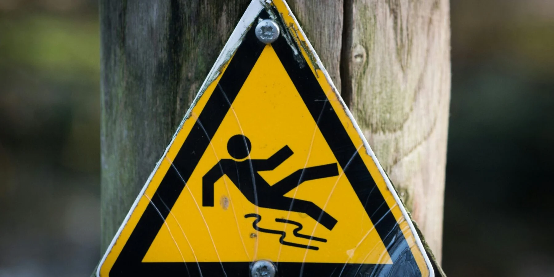 Yellow slip hazard warning sign mounted on a wooden post